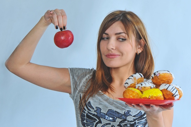 Девушка держит в руках яблоко и тарелку с пончиками