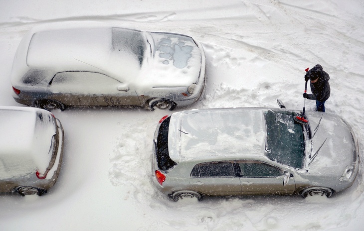 Мужчина чистит автомобиль от снега.